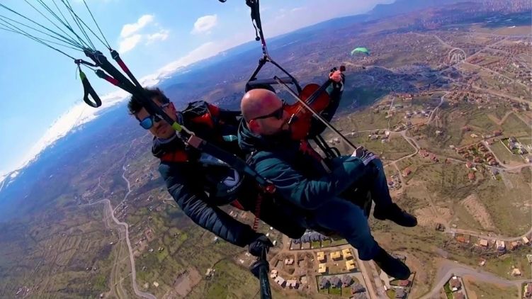 Man plays violin while paragliding